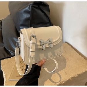 Detail van een crèmewitte leren crossbodytas met een grote zilveren metalen strikgesp