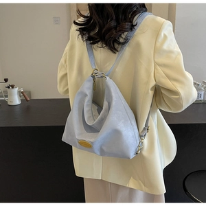 Détail du sac hobo bleu clair texturé avec logo doré sur un blazer jaune