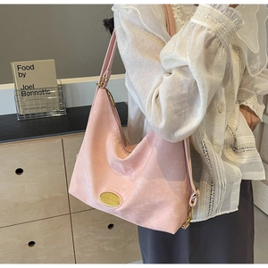 Détail du sac hobo en daim rose avec plaque logo et accents en métal doré