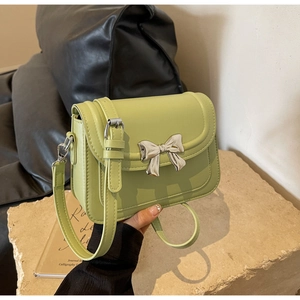 Detail van de avocado groene PU-leren tas met een zilveren metalen strik en schouderriem