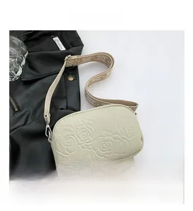 Detail of cream crossbody bag featuring 3D rose embossing and patterned textile strap
