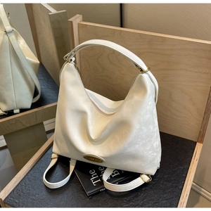 Détail du sac fourre-tout crème avec logo doré et texture de cuir souple sur fond bois