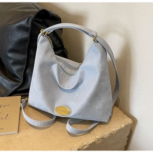 Détail du sac hobo bleu-gris clair avec plaque dorée sur une surface en pierre texturée