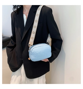 Detail of light blue crossbody bag with embossed rose texture and geometric woven strap