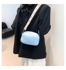 Detail of light blue crossbody bag featuring embossed roses and embroidered strap