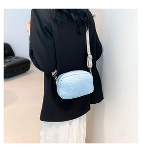 Detail of light blue crossbody bag with rose embossing and jacquard strap on model