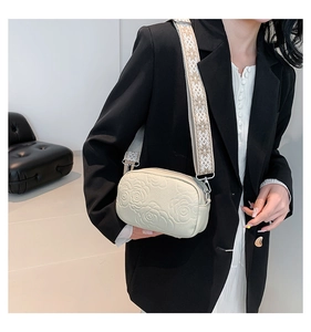 Detail of cream square crossbody bag with rose embossing and jacquard strap over black blazer