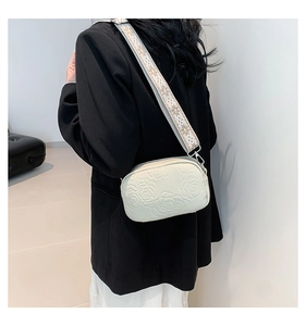 Detail of cream crossbody bag featuring 3D rose embossing and jacquard strap