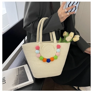 Detail of woven straw tote bag featuring colorful pom-poms and spacious interior design