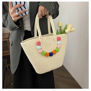 Detail of a large woven beach tote bag featuring colorful pom-poms and sturdy handles