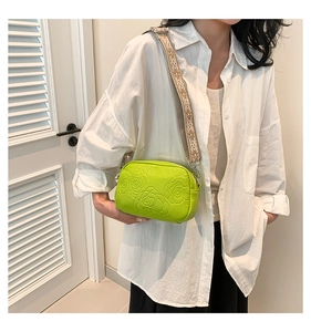 Detail of bright green crossbody bag featuring floral texture and ethnic woven strap