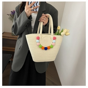 Close-up of beige woven tote bag with colorful pom-pom decor and cylindrical handles