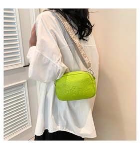 Detail of lime green embossed rose pattern on crossbody bag with wide woven strap