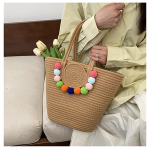 Detail of woven straw tote bag featuring colorful pom-pom decor and natural texture
