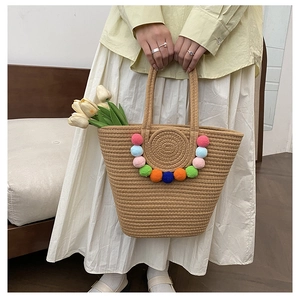 Detail of woven straw beach tote bag featuring vibrant colorful pom-pom decorations