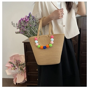 Detail of handwoven straw tote bag with colorful pom-pom fringe and woven handles