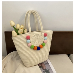 Close-up of cream woven tote bag with colorful pom-pom charms and cotton rope handles