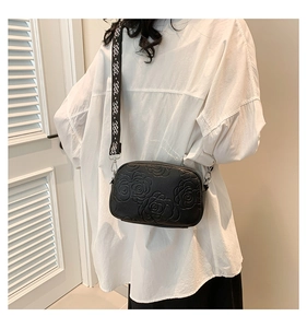 Detail of black crossbody bag with embossed floral pattern and wide woven geometric strap