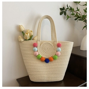 Detail of woven straw tote bag featuring colorful pom-pom trim and round patterns
