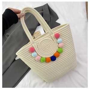 Detail of woven straw tote bag featuring colorful pom-pom decor and textured cotton rope