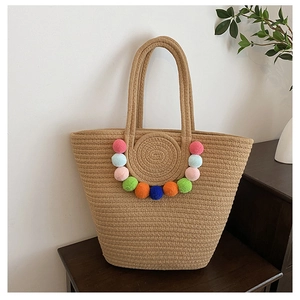 Detail of woven straw beach tote bag featuring vibrant colorful pom-poms on the front