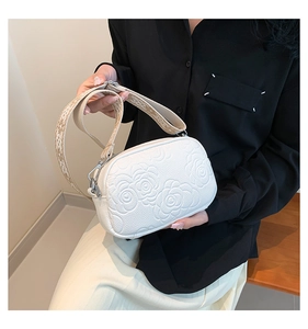 Close-up of white crossbody bag with camellia flower embossing and wide strap