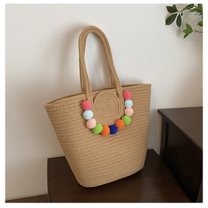 Detail of hand-woven straw tote bag featuring colorful pom-poms and sturdy dual handles