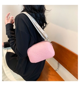 Close-up of pink crossbody bag with embossed rose pattern and woven strap detailing