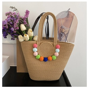 Detail of woven straw tote bag featuring colorful pom-pom trim and sturdy handles