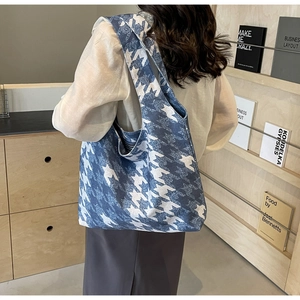 Detail view of blue and white houndstooth canvas tote bag worn by a model in a modern room