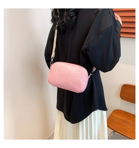 Detail of pink crossbody camera bag with embossed rose floral pattern and woven strap
