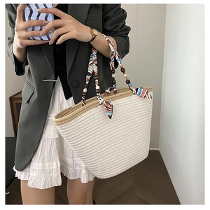 Detail view of woven straw tote bag featuring silk scarf handle and wooden bead charms