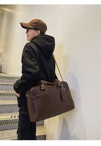 Detail of a large brown leather tote bag with hand straps and adjustable shoulder strap