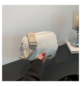 Detailed view of white crossbody camera bag with rose embossing and wide embroidered strap