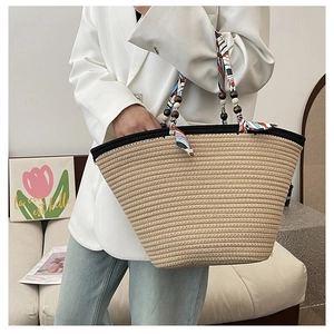Detail of woven straw tote bag featuring silk scarf handle and wooden bead accents