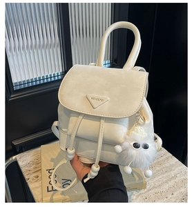 Close-up of a white leather mini backpack with a metal logo and a plush monster charm