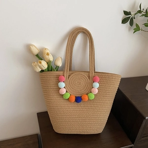 Handwoven straw tote bag with colorful pom-pom trim and large capacity for beach vacations