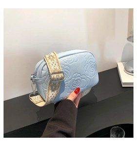 Detail of light blue crossbody bag with embossed rose texture and wide woven strap