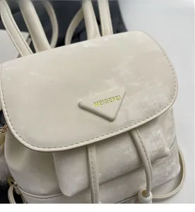 Detail of ivory mini backpack featuring flap closure with triangle logo and plush ball charm