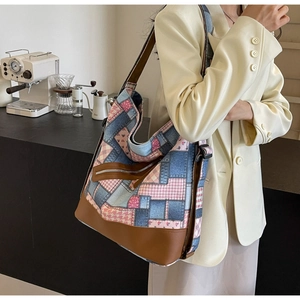 Detail of patchwork denim tote bag with leather base and floral accents on model