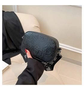 Detail of black crossbody bag with embossed rose floral texture and patterned strap