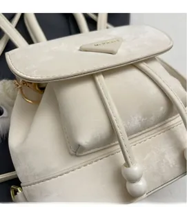Close-up of beige suede backpack with triangle logo, drawstring and plush ball charm