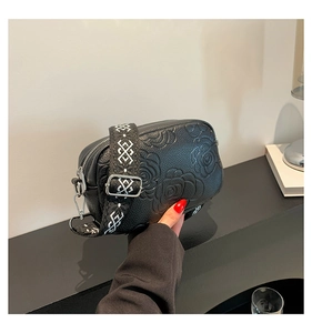 Detail of black lychee leather crossbody bag with rose embossing and jacquard wide strap