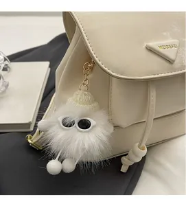 White fuzzy monster bag charm with sunglasses on a minimalist cream leather backpack