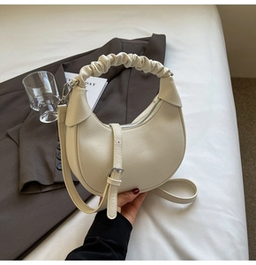 Detail shot of a creamy white crescent bag featuring lychee texture and pleated handle