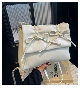 Détail du sac bandoulière blanc crème plissé avec deux nœuds et logo de la marque