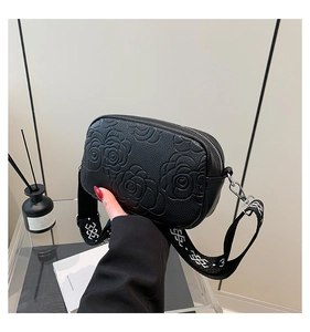 Detail of black camellia embossed leather crossbody bag with geometric wide strap