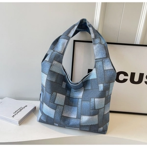 Detail of a blue patchwork canvas tote bag with wide straps in a minimalist studio setting