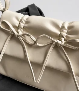 Détail du sac en cuir plissé crème avec un nœud élégant et le logo de la marque
