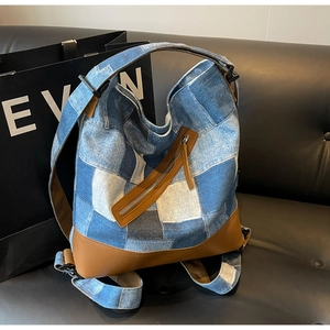 Detail of blue denim patchwork backpack with brown leather trim on black leather sofa